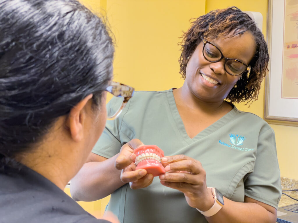 Dentist showing a full-arch denture model to a patient at ReNew Dental Care
